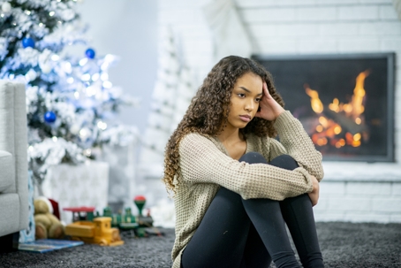 A woman sits near a fireplace and Christmas tree dealing with holiday stress during a divorce