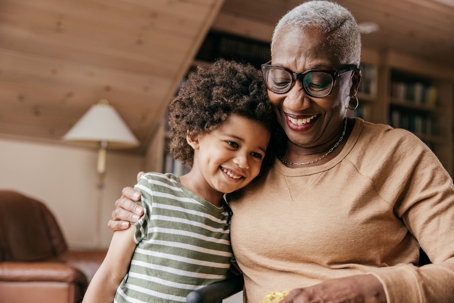 A smiling grandmother hugs her smiling young grandson.