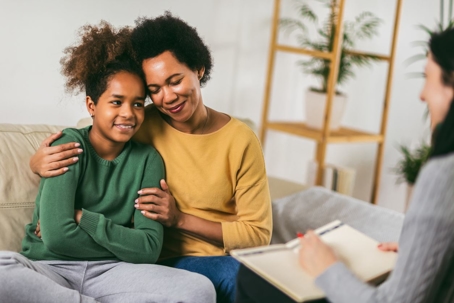 A mother hugs her daughter on a couch during a therapy session.
