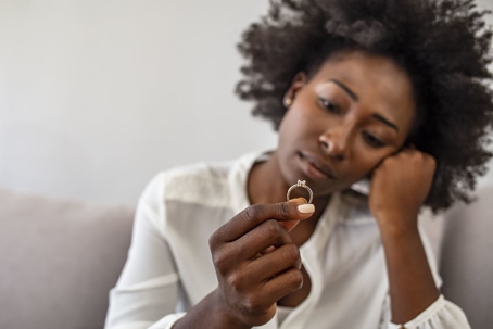 A sad woman holds her wedding ring looking depressed.