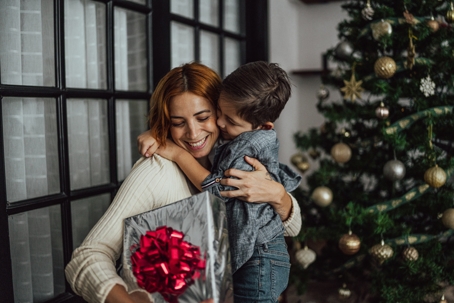 A mother hugs her son near a Christmas tree during the holidays