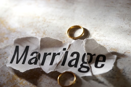 A shredded paper reading "MARRIAGE" reassembled on a table with two wedding rings on either side.