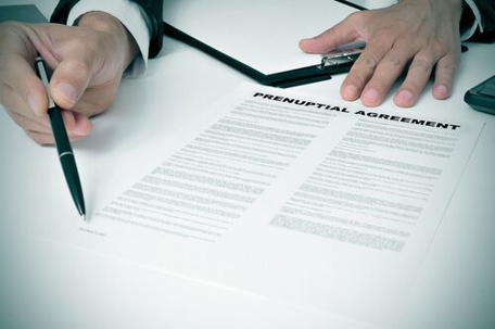 A person's hands holding a pen and pointing to sign a prenuptial agreement.
