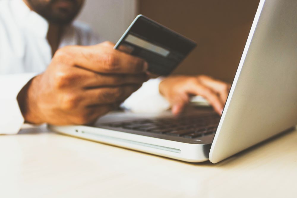 Close up of one hand holding a credit card and the other typing on a laptop to pay San Diego child support.