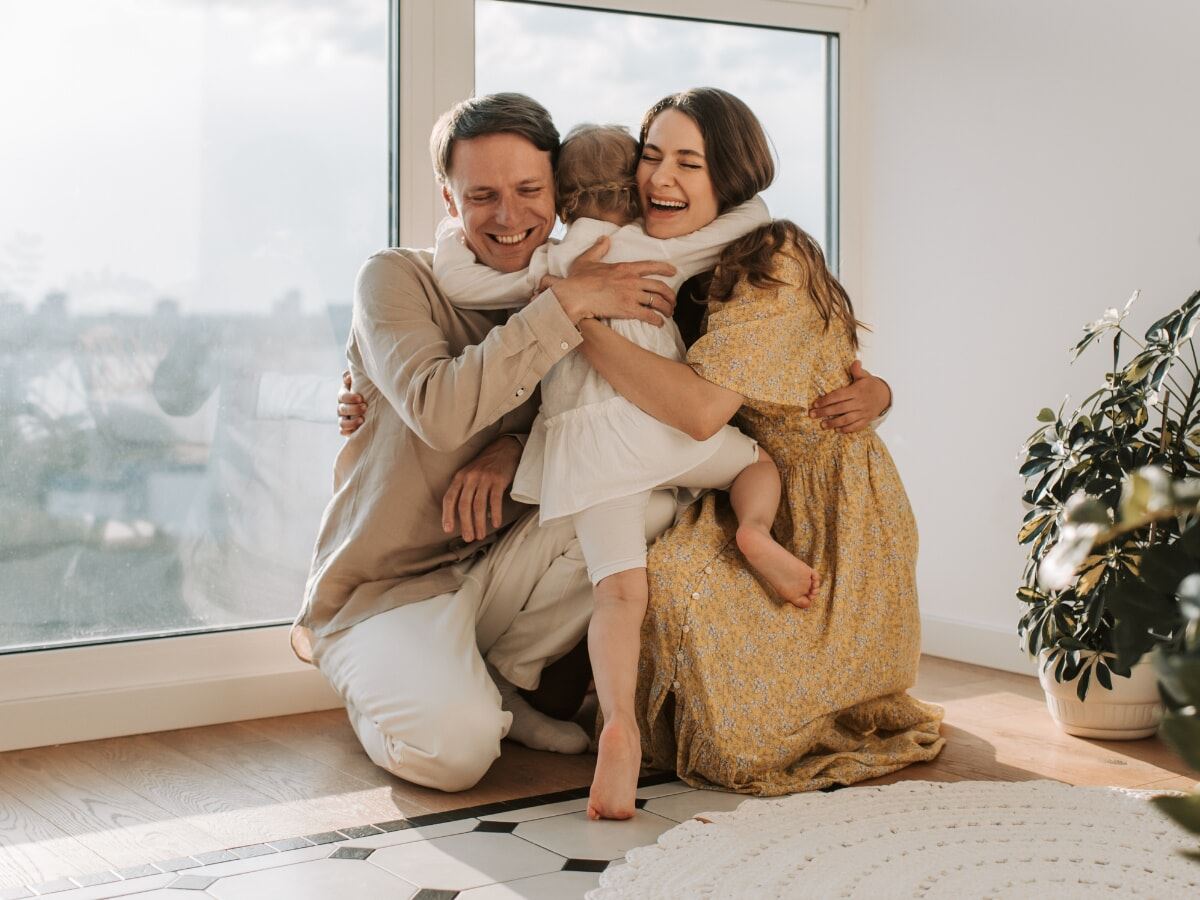 San Diego parents kneeling and laughing while hugging adopted child.